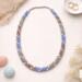 Handcrafted Kumihimo beaded necklace arranged in styled flat lay, blue, mauve, silver and white tones with soft neutral accents